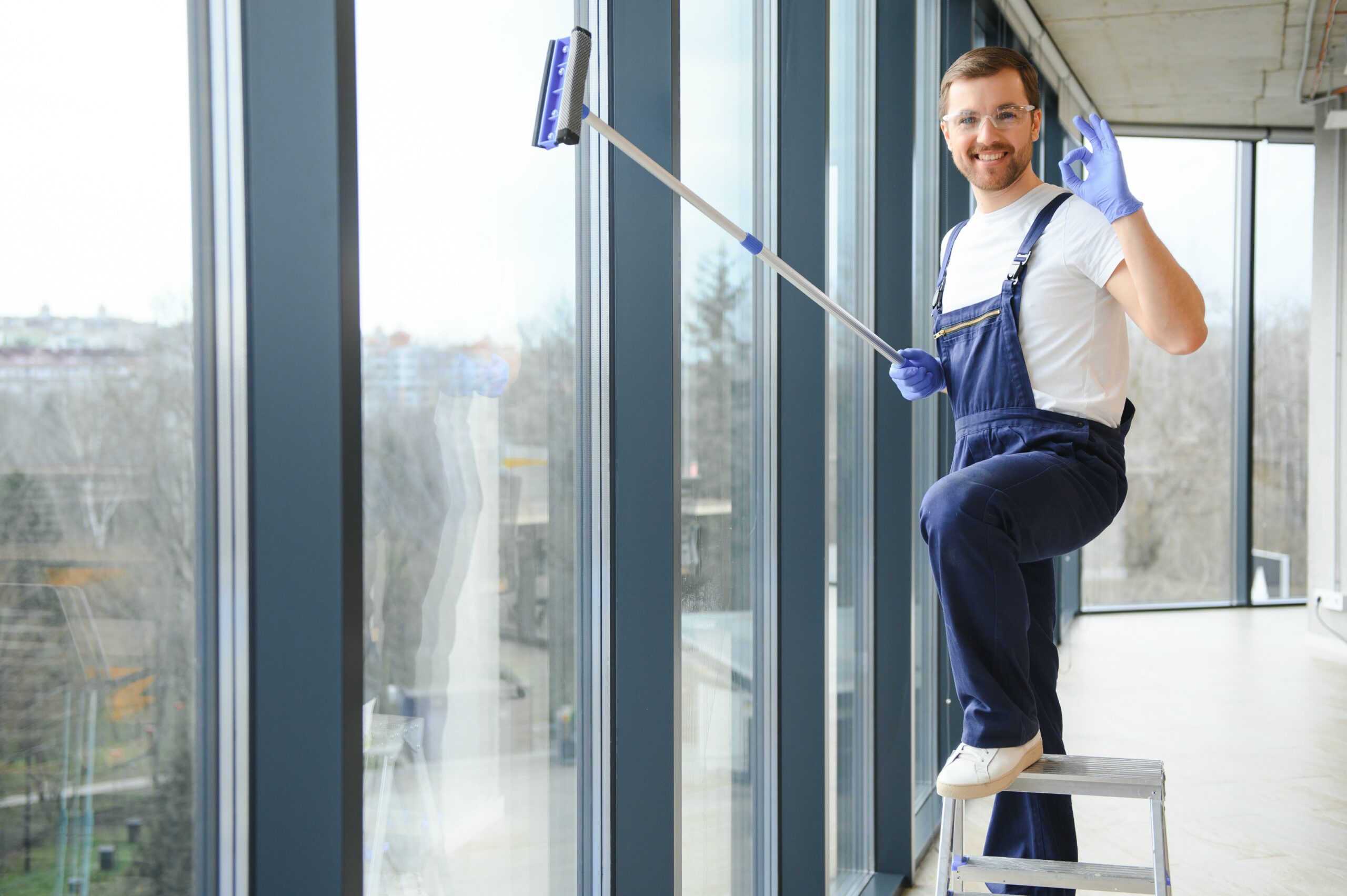 Male professional cleaning service worker in overalls cleans the windows and shop windows of a store with special equipment