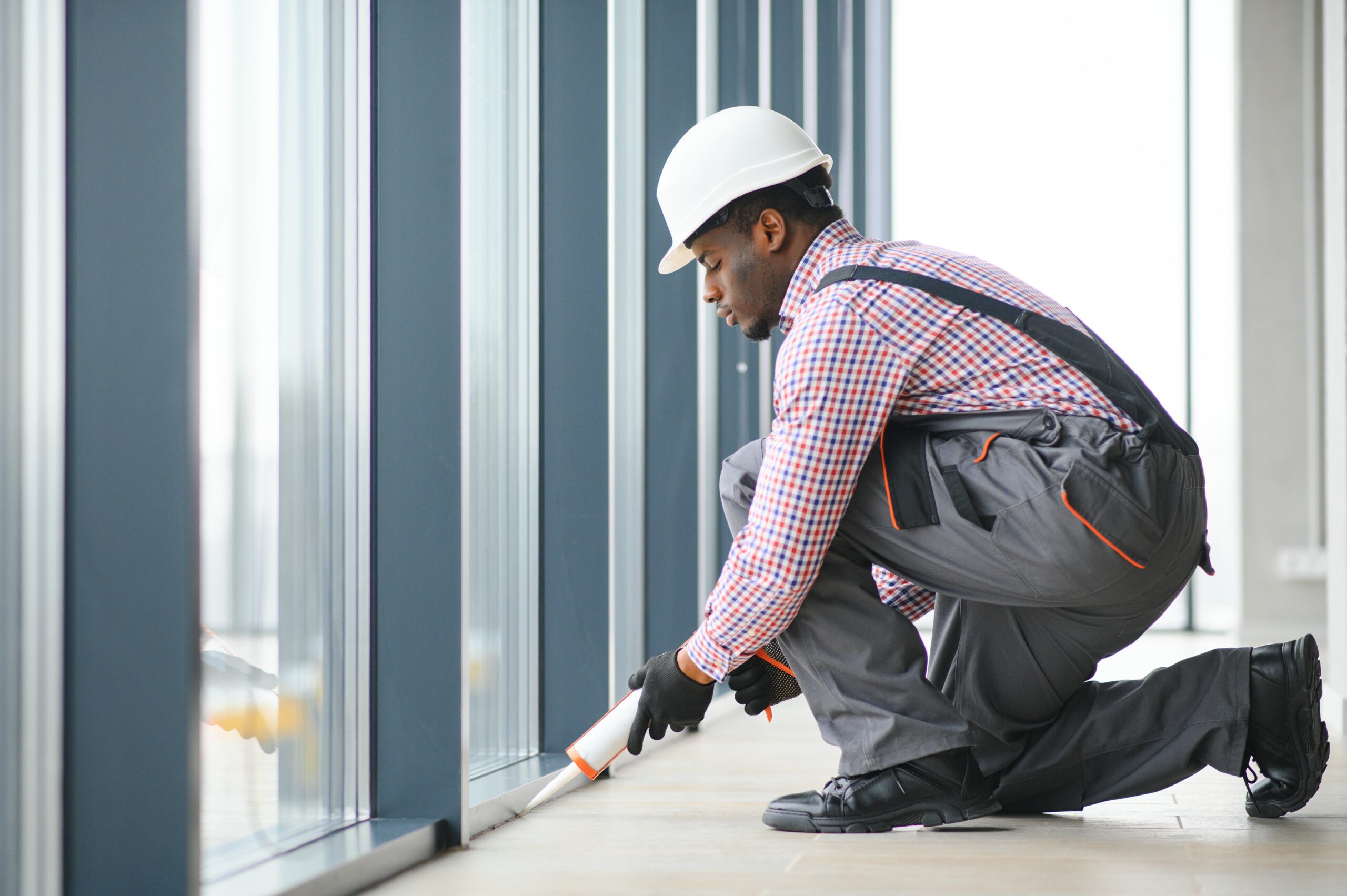 Workman in overalls installing or adjusting plastic windows in the living room at home