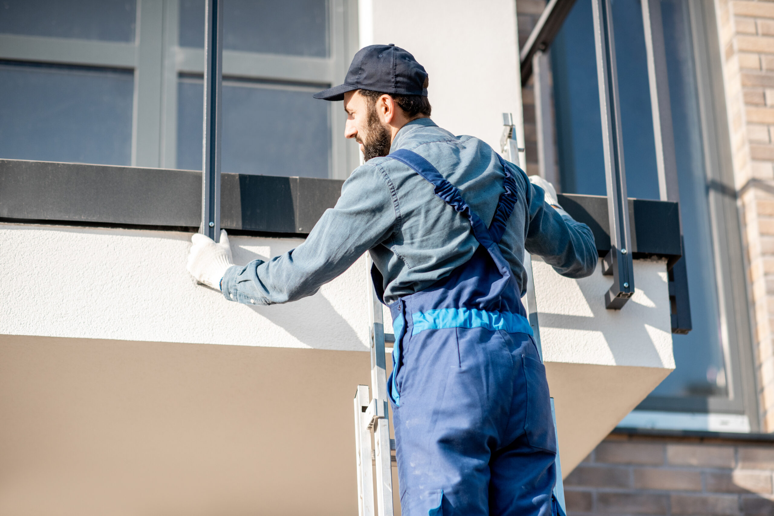 Builder in blue uniform mounting aluminium fence on the balcony of the new building