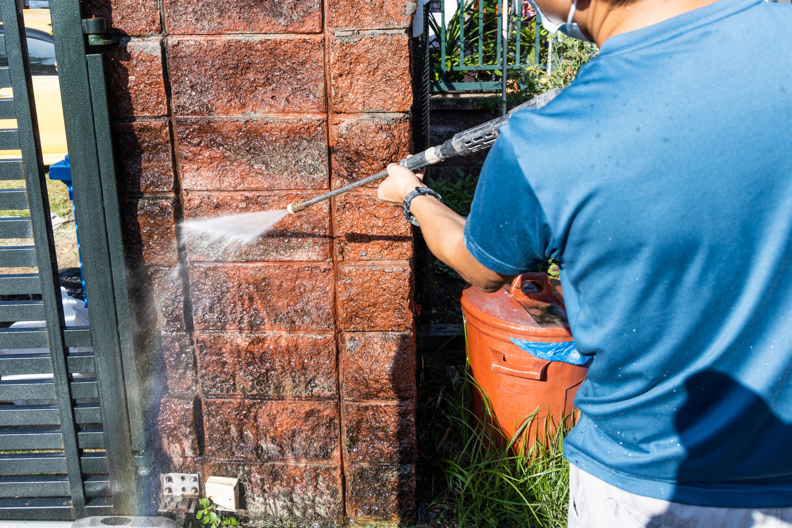 Worker using high pressure water jet spray gun to wash and clean dirty wall with moss at residential building in renovation