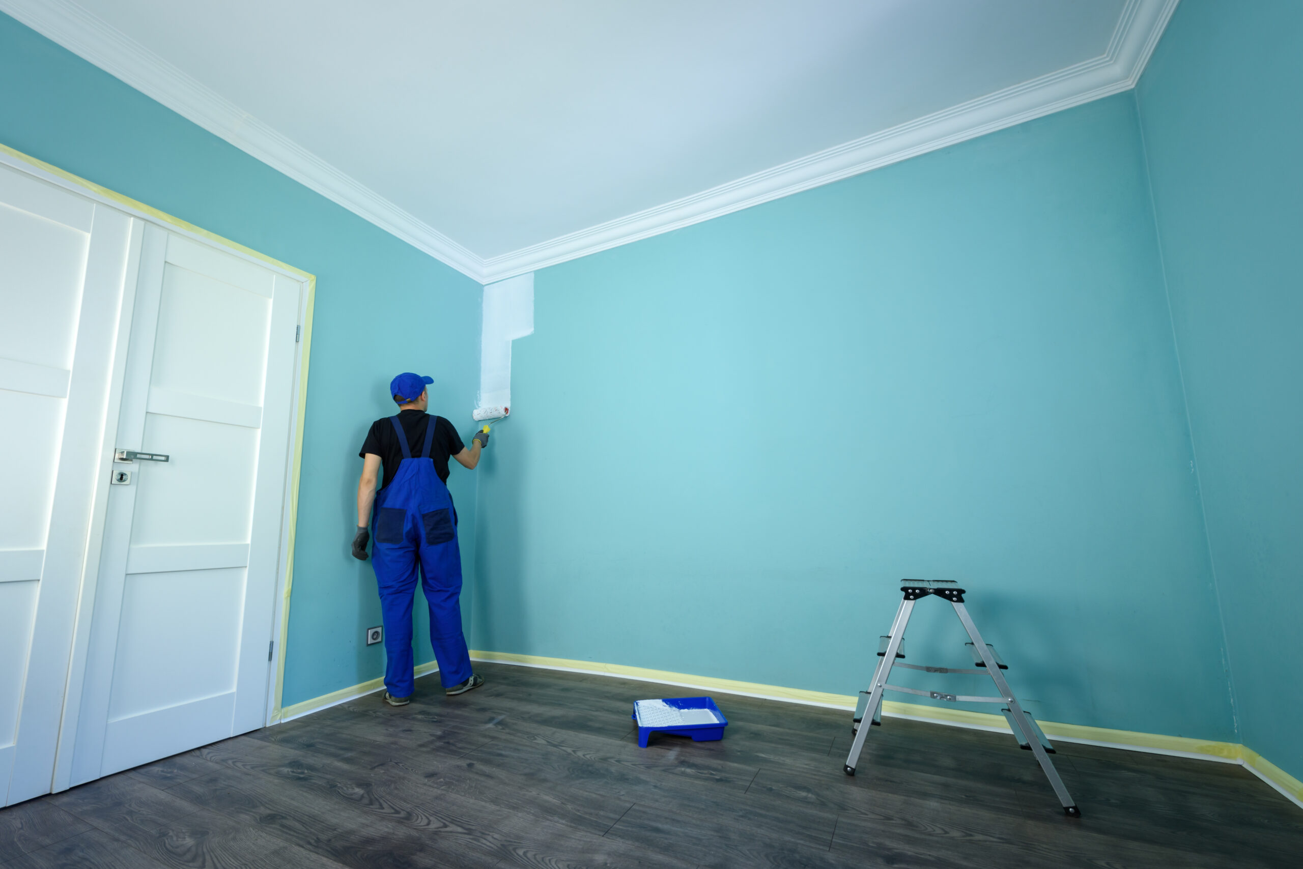 Man in a working overall is painting the wall in white color