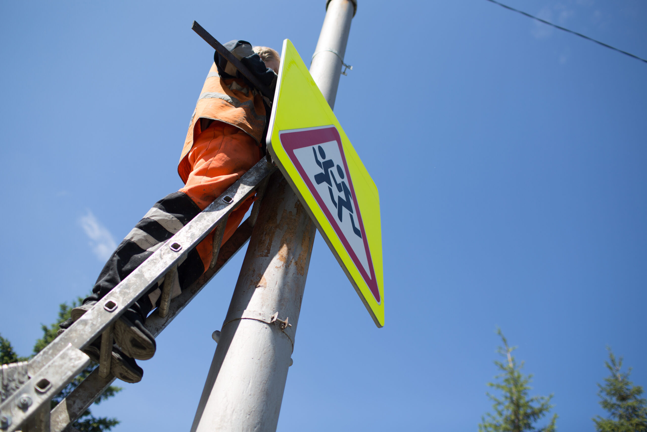 Installation road sign on pole. Road worker sets sign on blue sky background.