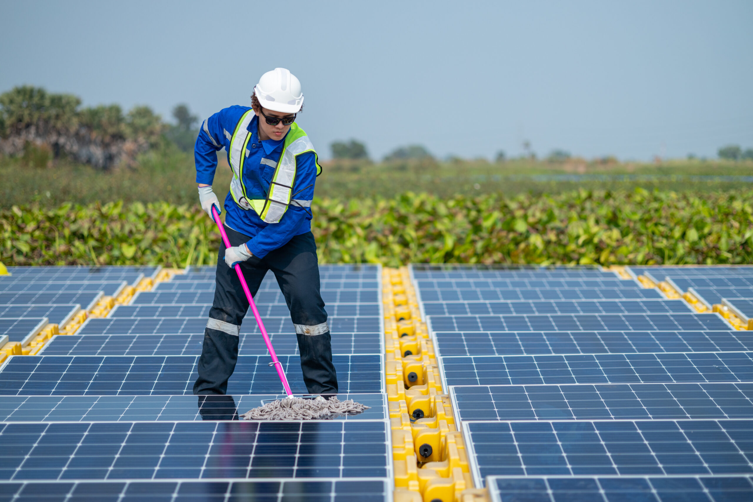 A worker in protective equipment meticulously cleans the surface of solar panels to ensure maximum efficiency at a solar farm.