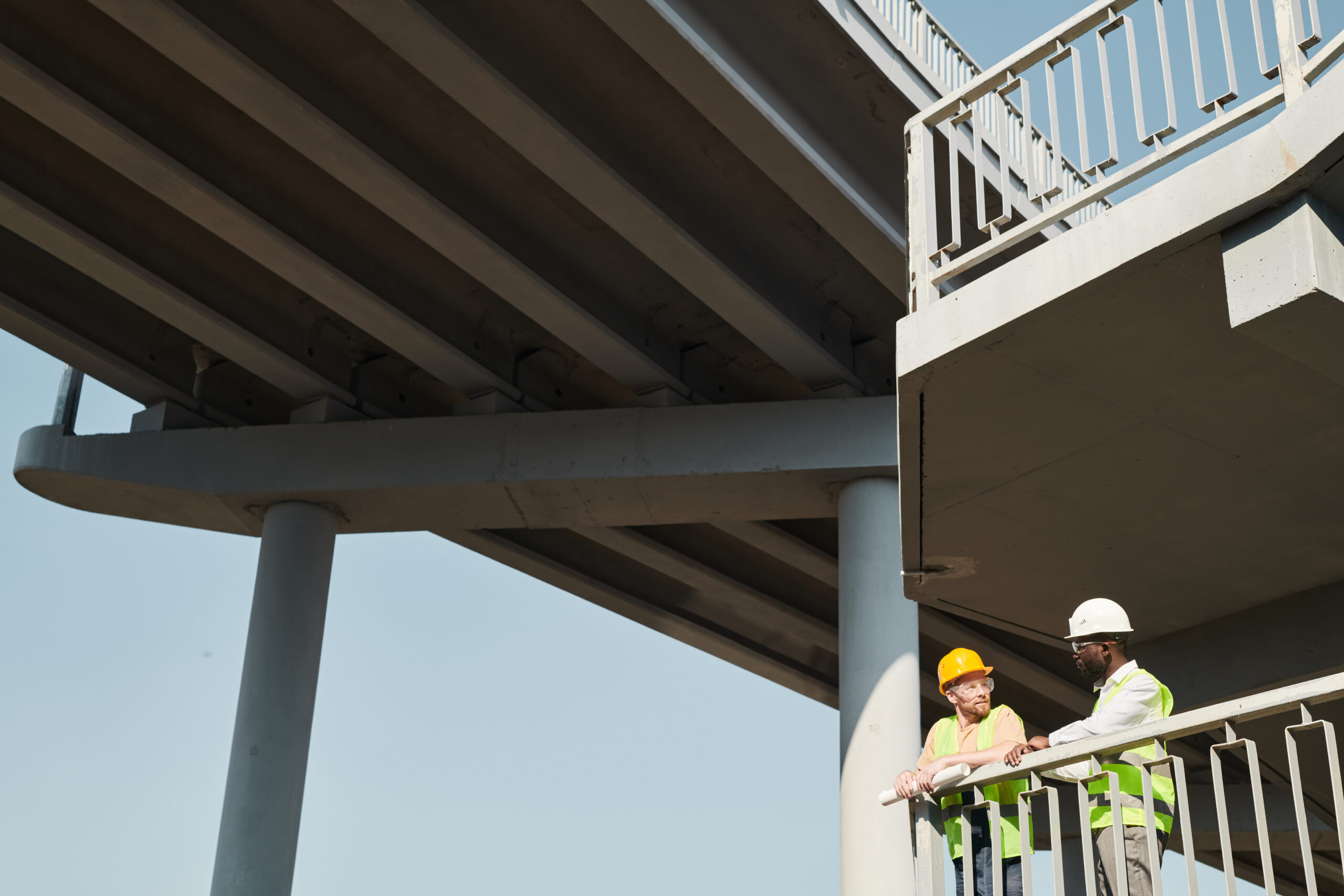 Professional engineers in workwear standing at construction site and discussing building process