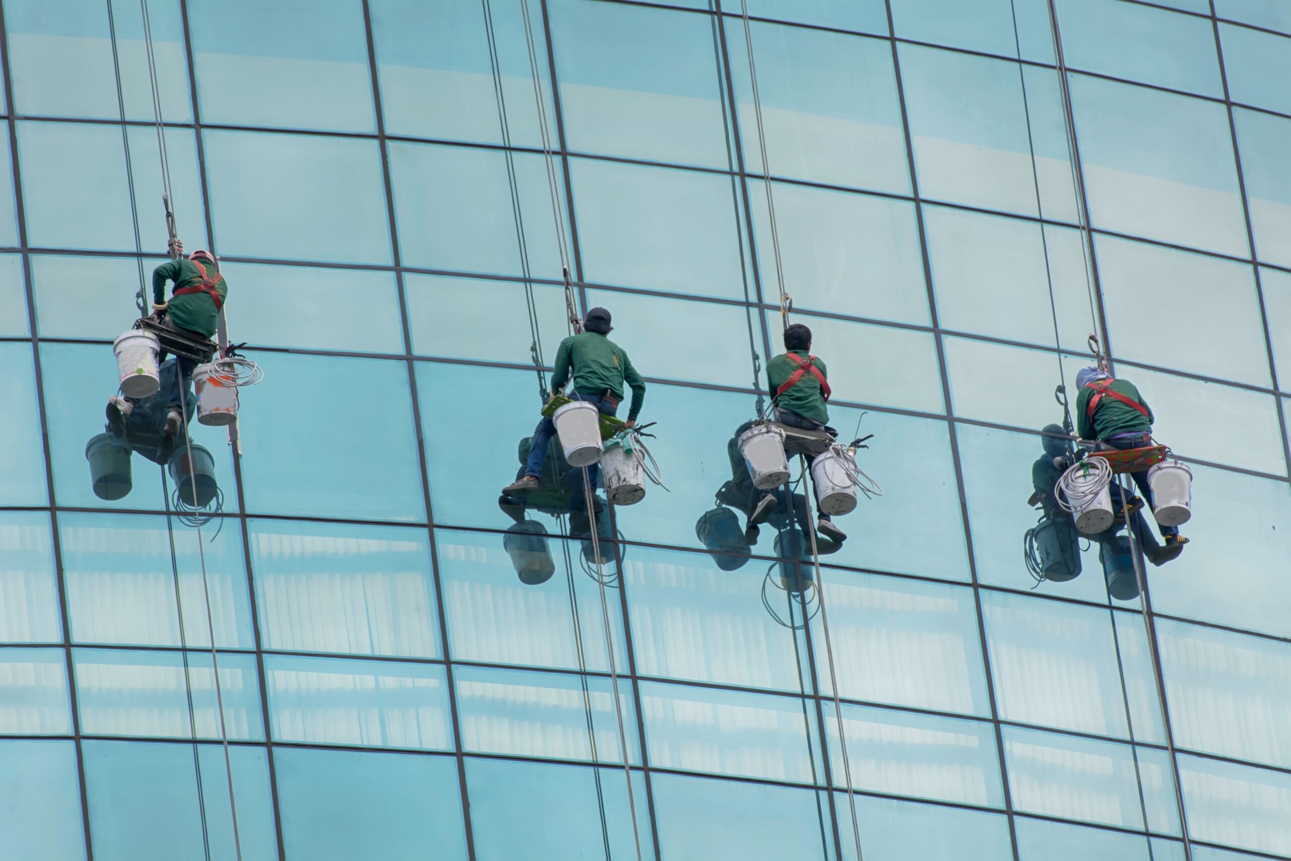 The workers hanging down while cleaning the glass windows of the skyscraper