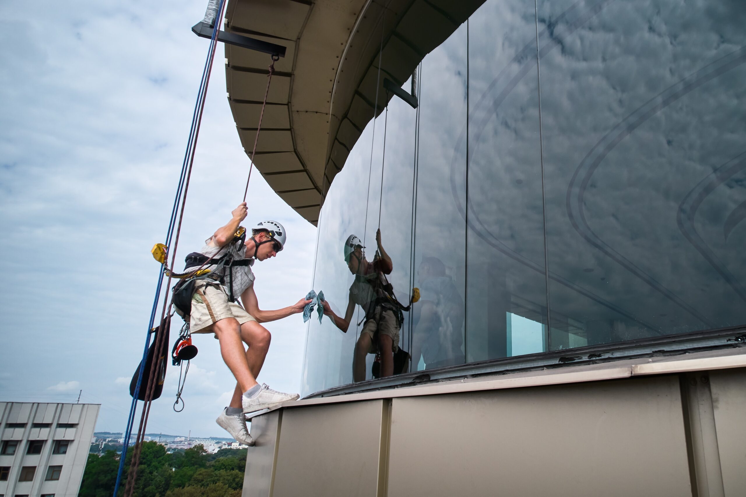 Industrial mountaineering worker professional cleaner hanging on climbing rope and cleaning window of high-rise building. Window washer using safety lifting equipment while washing skyscraper facade.