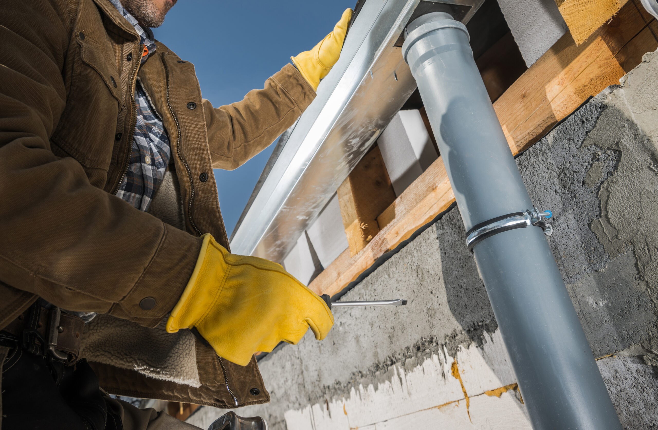 Construction Worker Finishing Installation of Eaves Roof Gutters. Industrial Theme.