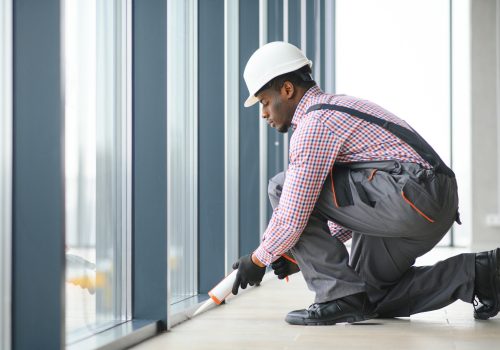 Workman in overalls installing or adjusting plastic windows in the living room at home