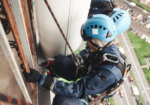 Two industrial mountaineering laborers in uniform and helmets hanging over residential building facade. Workers working on wall, access high rise work. Industry urban work concept. Copy ad text space